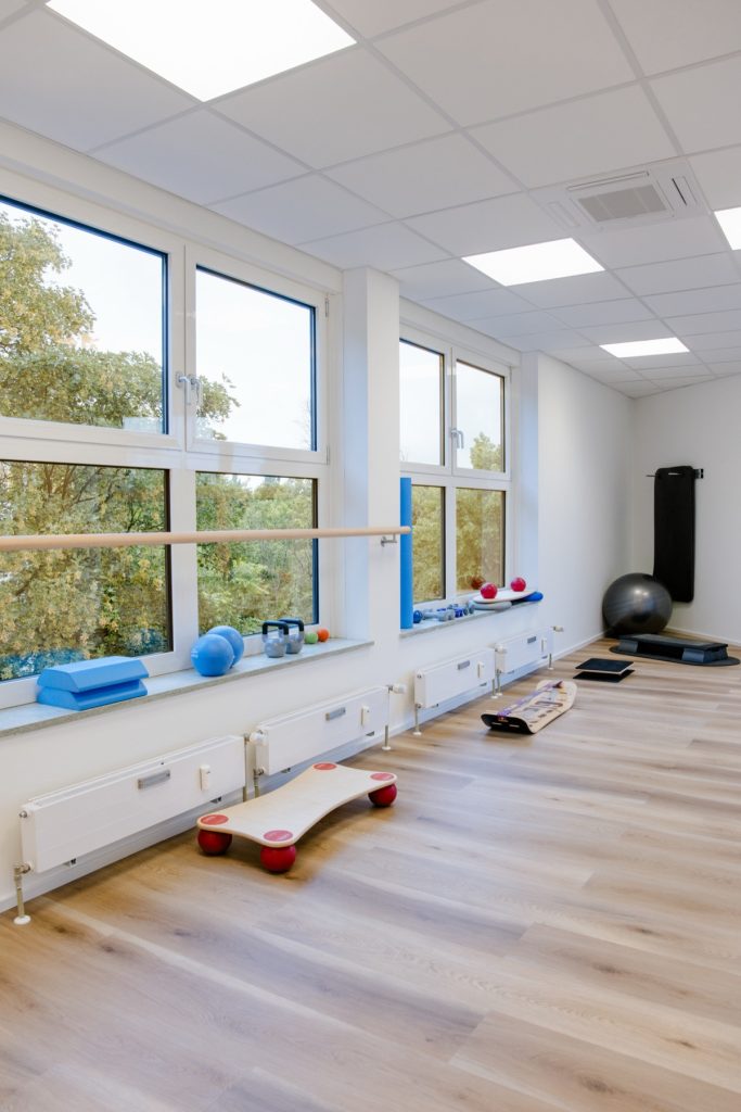 Praxisraum mit Balance-Boards und Therapiegeräten am Fenster